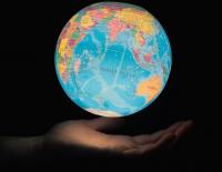 illuminated globe above an upturned hand against a black background